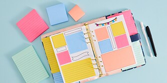 Un agenda ouvert avec des notes Post-it® colorées, entouré de notes Post-it® de différentes tailles, de couleur rose, bleu et pêche
