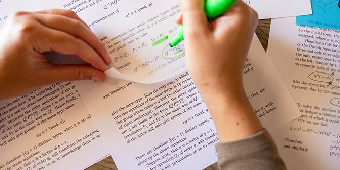 Étudiant surlignant du texte sur des pages imprimées à l'aide d'un surligneur et de notes Post-it® transparentes, en se concentrant sur les équations mathématiques

