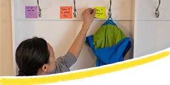 Une mère plaçant des Notes Post-it® colorées avec des messages positifs et les collant à côté des crochets dans le couloir
