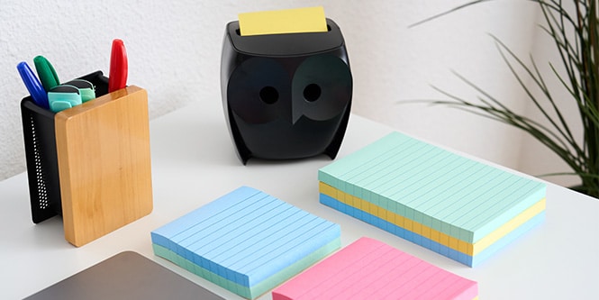Un bureau avec des notes Post-it® de différentes couleurs, un porte-stylo et un dévidoir de notes Post-it® en forme de hibou

